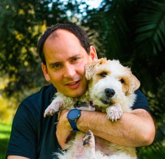 Cheerful man and fluffy dog playing in a sunny park, enjoying nature and companionship.